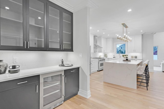 kitchen with wall chimney exhaust hood, stainless steel range, white cabinets, and wine cooler