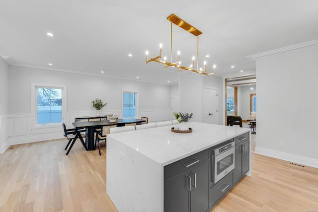 kitchen featuring stainless steel microwave, crown molding, light hardwood / wood-style flooring, a center island, and hanging light fixtures