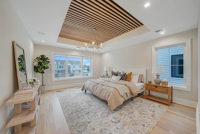 bedroom featuring a tray ceiling, light hardwood / wood-style floors, and a notable chandelier