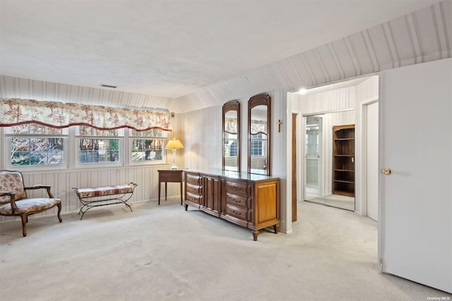 sitting room featuring wood walls, light colored carpet, and a healthy amount of sunlight