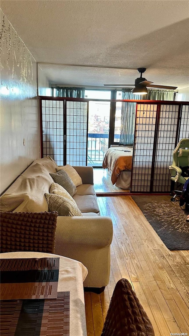 living room featuring wood-type flooring, a textured ceiling, floor to ceiling windows, and ceiling fan