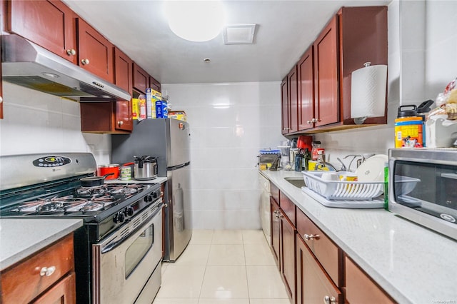 kitchen with light stone counters, light tile patterned flooring, tile walls, and appliances with stainless steel finishes