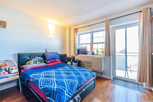 bedroom with access to exterior, wood-type flooring, and a textured ceiling