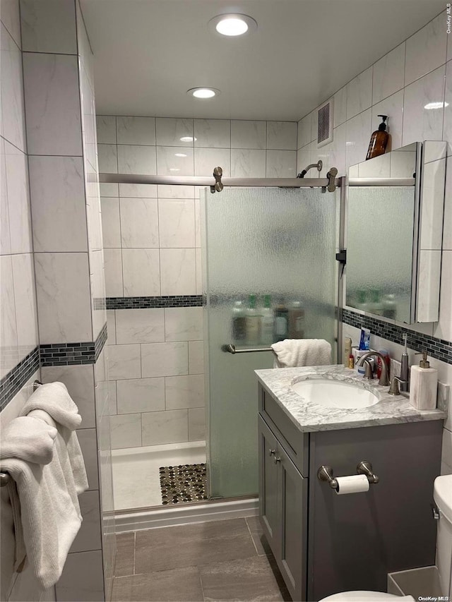 bathroom with vanity, toilet, a shower with door, and tile walls