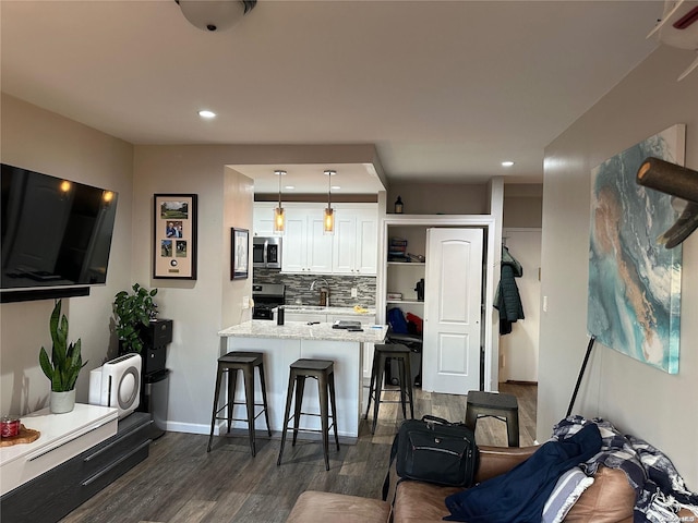 kitchen with kitchen peninsula, a breakfast bar, stainless steel appliances, dark wood-type flooring, and white cabinetry