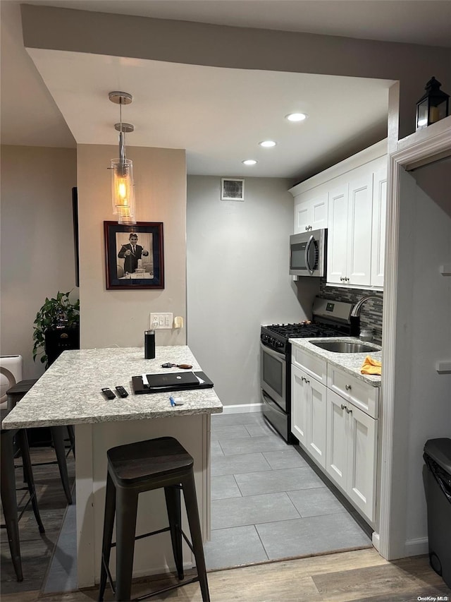 kitchen with a kitchen bar, stainless steel appliances, sink, light hardwood / wood-style floors, and white cabinetry