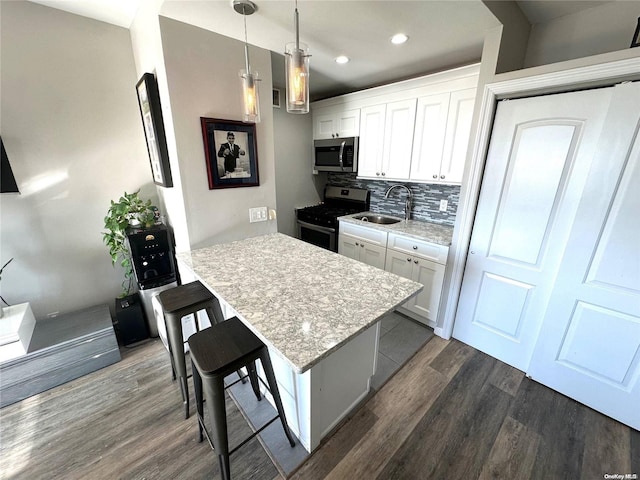 kitchen with a kitchen bar, stainless steel appliances, dark wood-type flooring, white cabinets, and hanging light fixtures