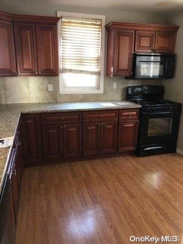 kitchen with light stone countertops, dark hardwood / wood-style flooring, backsplash, and black appliances