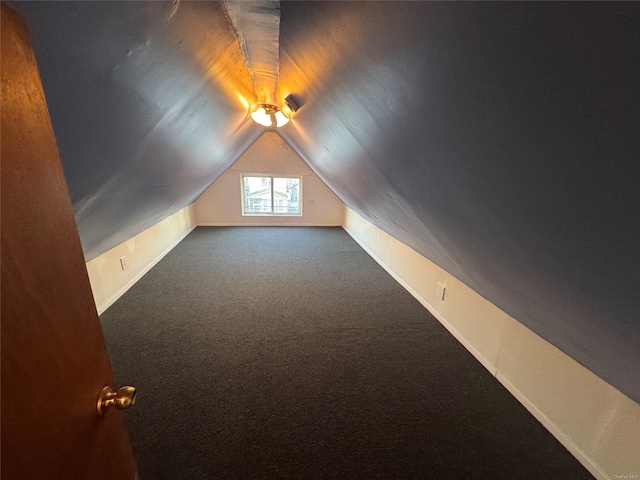 bonus room with dark colored carpet and lofted ceiling