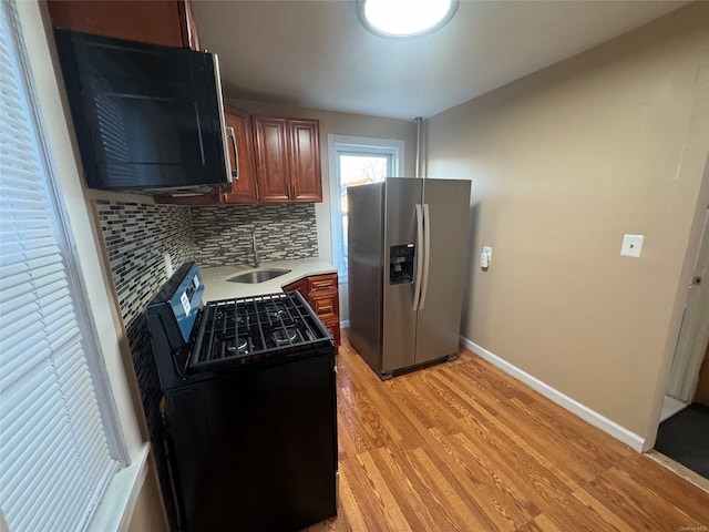 kitchen with black electric range oven, backsplash, sink, stainless steel fridge, and light wood-type flooring