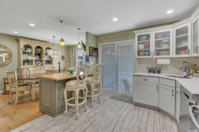 kitchen featuring white cabinetry, sink, decorative light fixtures, and light hardwood / wood-style flooring