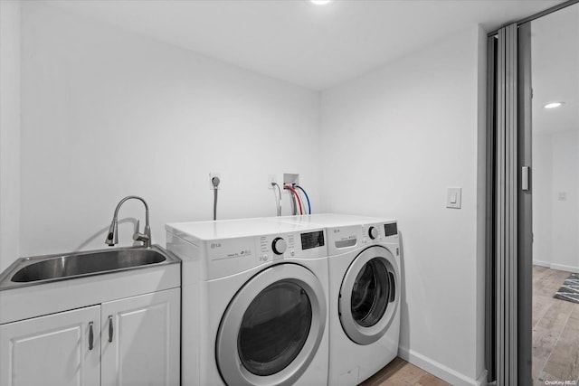 laundry area featuring washer and clothes dryer, cabinets, sink, and light hardwood / wood-style flooring