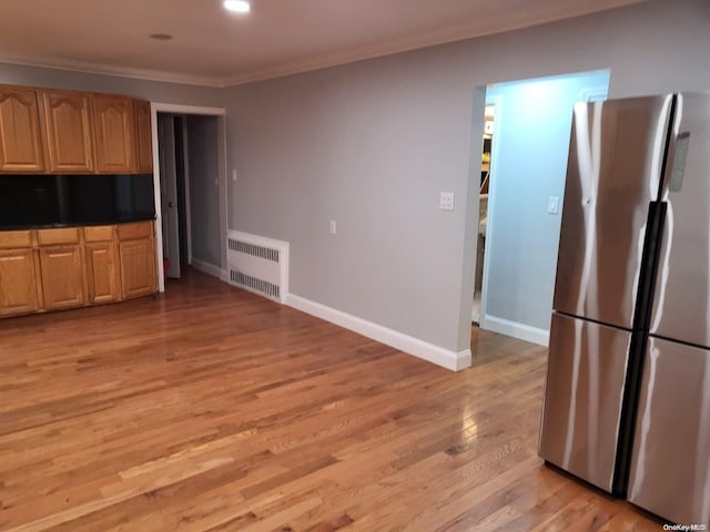 kitchen featuring radiator, light wood-type flooring, crown molding, and stainless steel refrigerator