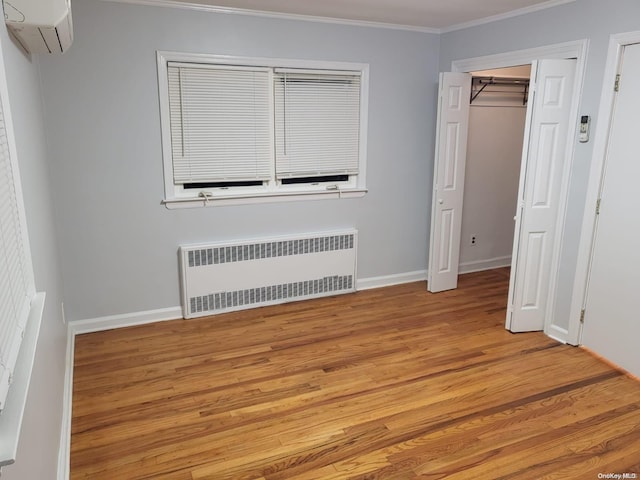 unfurnished bedroom featuring radiator, a wall unit AC, crown molding, light hardwood / wood-style floors, and a closet