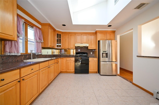 kitchen with a skylight, sink, dark stone counters, gas stove, and stainless steel refrigerator with ice dispenser