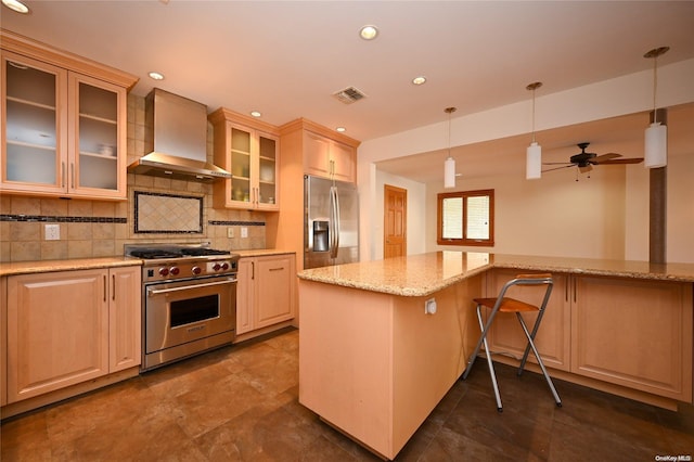 kitchen featuring wall chimney range hood, backsplash, hanging light fixtures, stainless steel appliances, and light stone counters