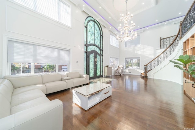 living room with dark wood-type flooring, an inviting chandelier, crown molding, a towering ceiling, and a tray ceiling