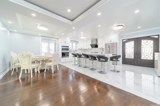 kitchen featuring french doors, a tray ceiling, a kitchen island, a kitchen bar, and white cabinetry