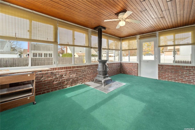 unfurnished sunroom featuring a wood stove, ceiling fan, and wooden ceiling