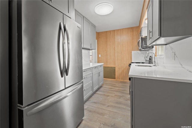 kitchen with light stone countertops, sink, stainless steel appliances, light hardwood / wood-style floors, and gray cabinets