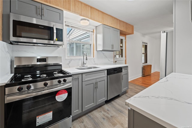 kitchen with light stone countertops, appliances with stainless steel finishes, sink, light hardwood / wood-style flooring, and gray cabinets