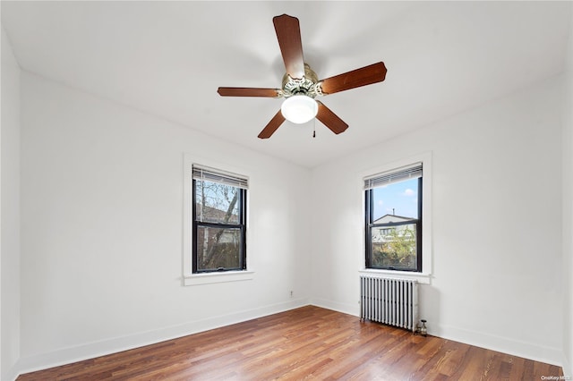 unfurnished room featuring radiator heating unit, ceiling fan, a wealth of natural light, and wood-type flooring