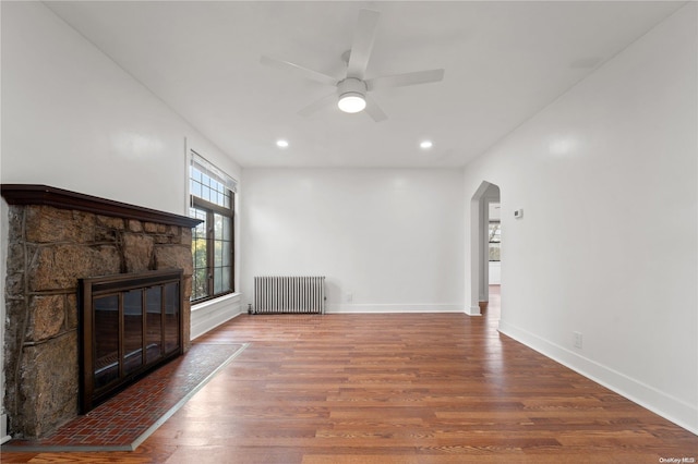 unfurnished living room featuring a fireplace, ceiling fan, radiator heating unit, and hardwood / wood-style flooring