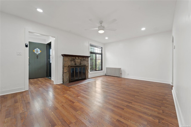 unfurnished living room featuring radiator, ceiling fan, hardwood / wood-style floors, and a fireplace