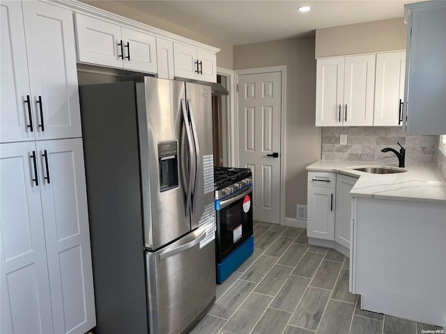 kitchen featuring sink, appliances with stainless steel finishes, white cabinetry, light stone countertops, and decorative backsplash