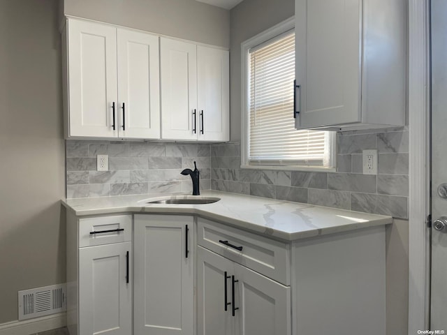 kitchen featuring backsplash, light stone countertops, sink, and white cabinets