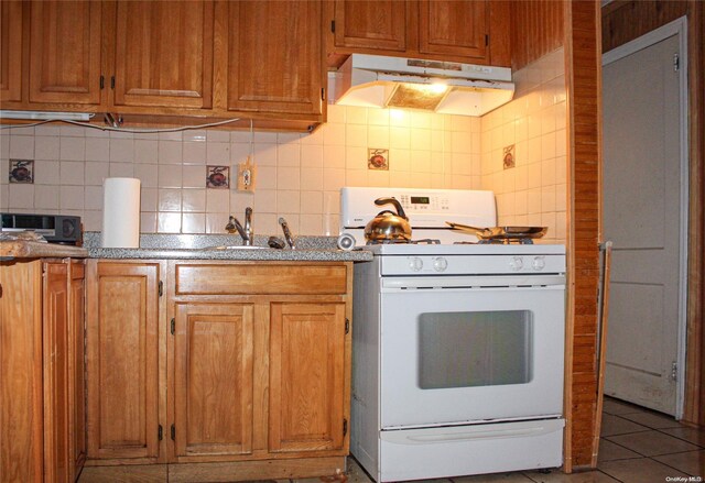 kitchen with tile patterned flooring, decorative backsplash, white range oven, and sink