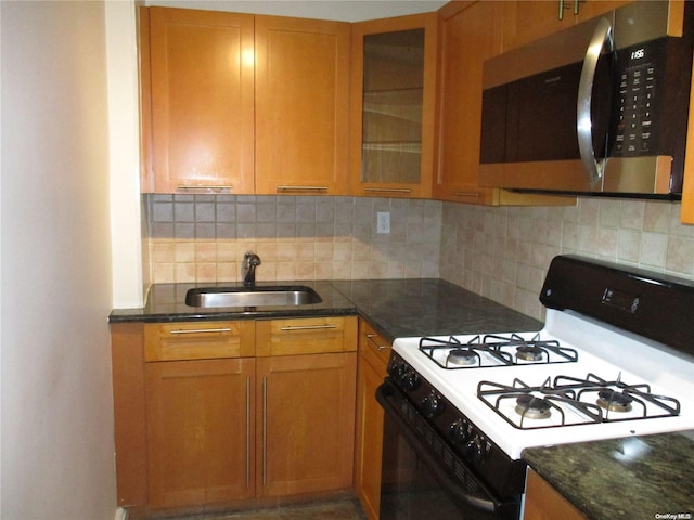 kitchen featuring decorative backsplash, sink, dark stone counters, and white gas range oven