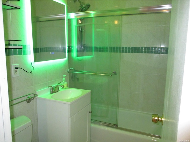 full bathroom featuring vanity, backsplash, bath / shower combo with glass door, toilet, and tile walls