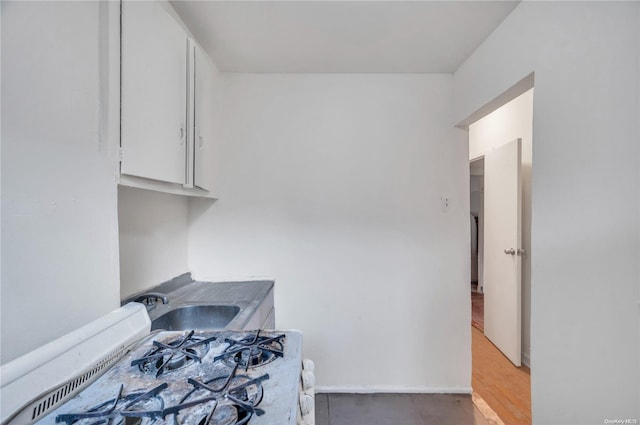 interior space with white cabinets, light hardwood / wood-style floors, sink, and gas range gas stove