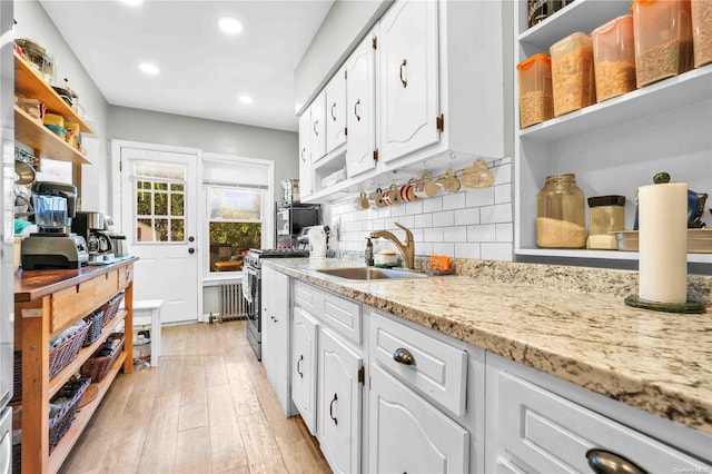 kitchen featuring light stone countertops, sink, backsplash, white cabinets, and light wood-type flooring