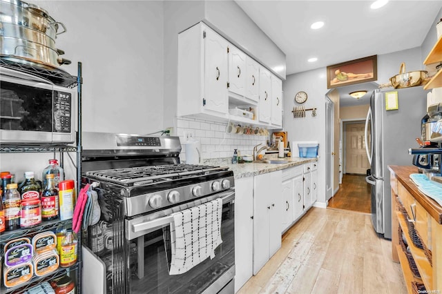 kitchen with backsplash, white cabinets, sink, light hardwood / wood-style floors, and stainless steel appliances