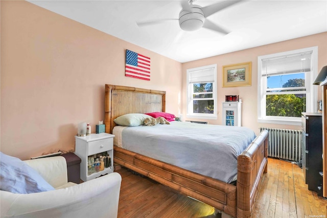 bedroom with radiator, ceiling fan, multiple windows, and hardwood / wood-style flooring