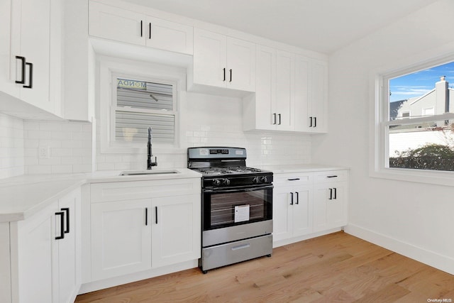 kitchen with white cabinetry, stainless steel gas stove, sink, light hardwood / wood-style floors, and decorative backsplash