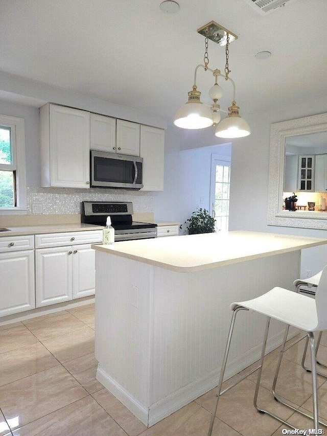 kitchen featuring white cabinetry, decorative light fixtures, decorative backsplash, light tile patterned floors, and range