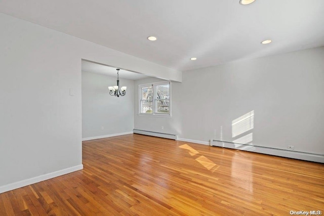 empty room with a baseboard heating unit, a notable chandelier, and light wood-type flooring