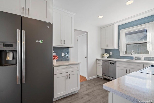 kitchen with sink, light hardwood / wood-style flooring, appliances with stainless steel finishes, white cabinets, and decorative backsplash