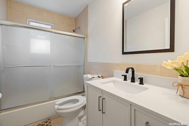 full bathroom featuring toilet, bath / shower combo with glass door, tile walls, vanity, and tile patterned flooring