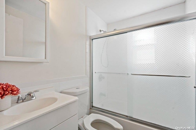 full bathroom featuring tile walls, vanity, bath / shower combo with glass door, and toilet