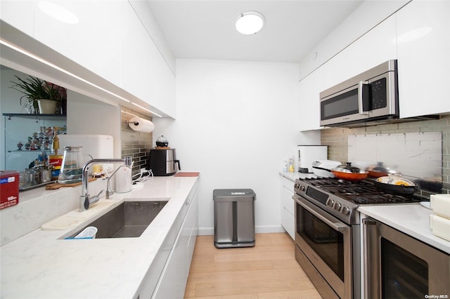 kitchen featuring white cabinets, appliances with stainless steel finishes, light wood-type flooring, and sink