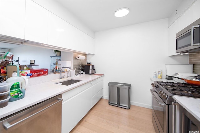 kitchen featuring white cabinets, sink, light hardwood / wood-style flooring, appliances with stainless steel finishes, and tasteful backsplash