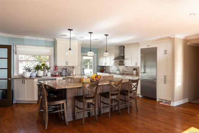 kitchen with appliances with stainless steel finishes, dark hardwood / wood-style flooring, light stone counters, wall chimney exhaust hood, and decorative light fixtures