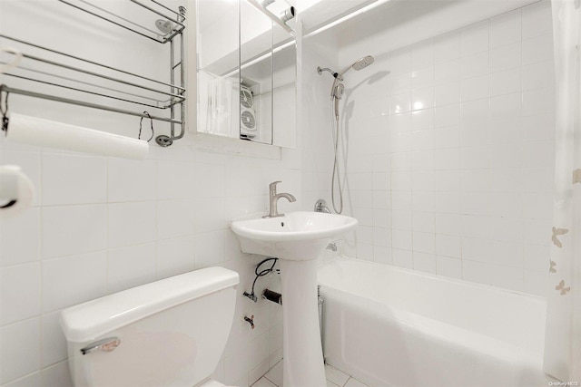 bathroom featuring tiled shower / bath combo, toilet, and tile walls