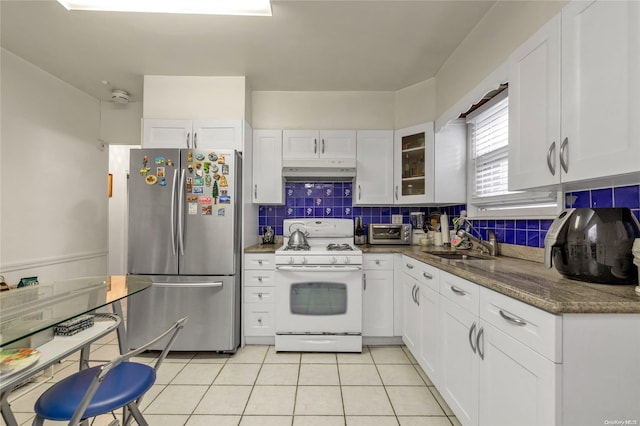 kitchen with dark stone counters, white cabinets, sink, stainless steel refrigerator, and white range with gas cooktop