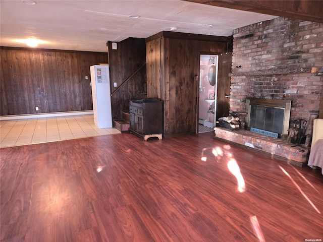 unfurnished living room with wood walls, a brick fireplace, and light wood-type flooring