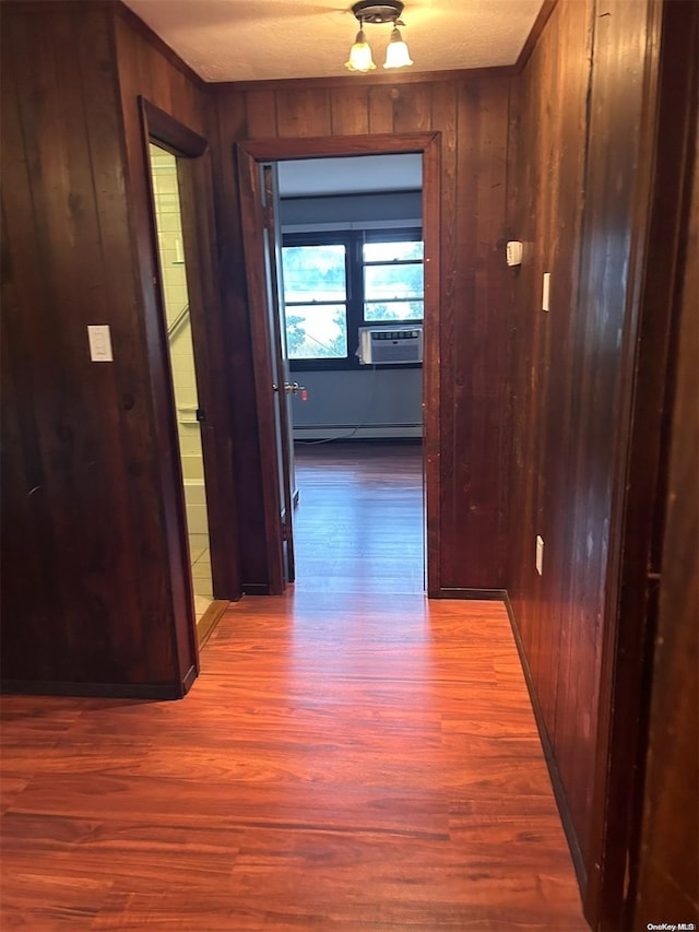 corridor with a baseboard radiator, hardwood / wood-style floors, and wood walls